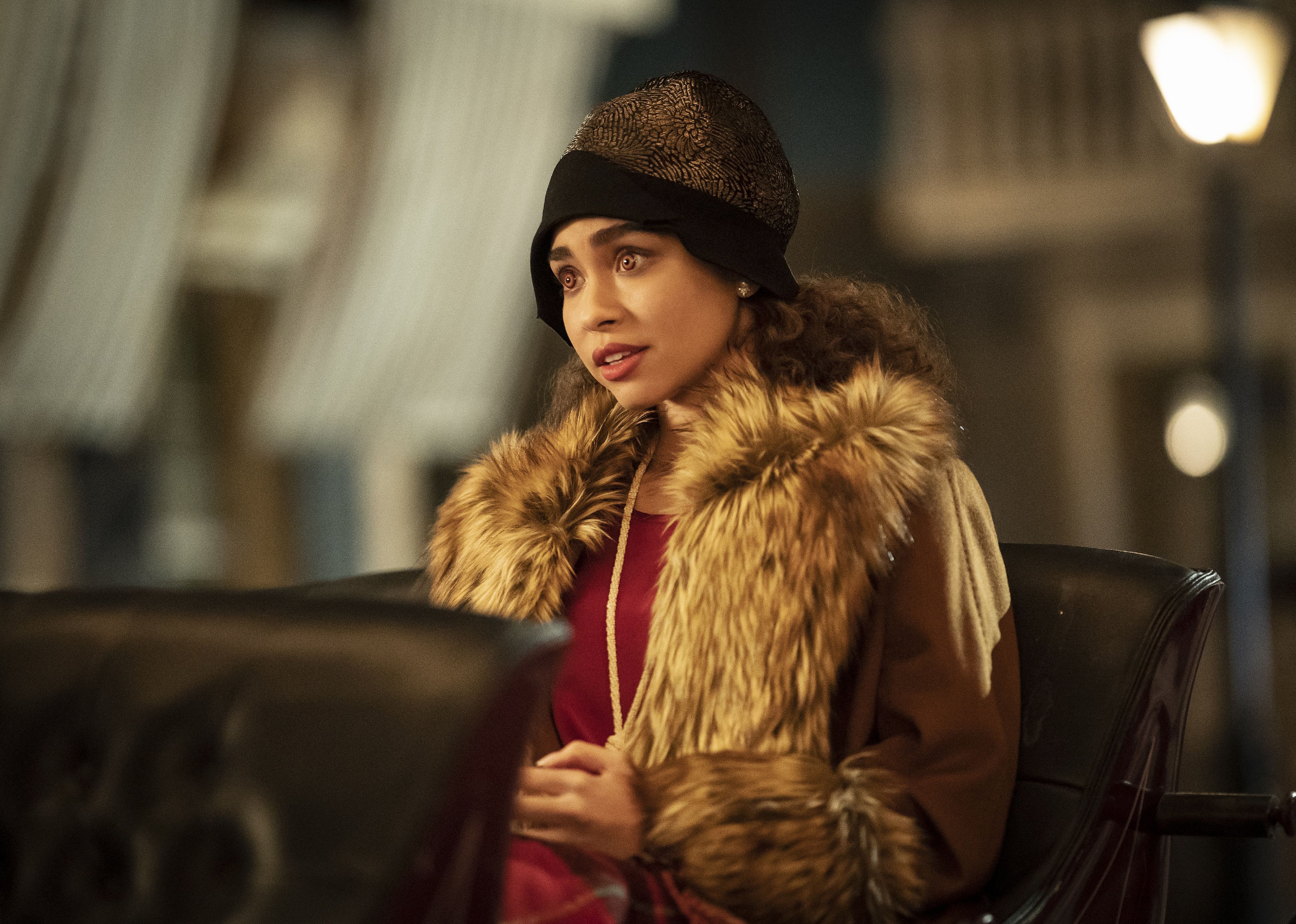 A young woman with red eyes wearing a fur and seated in a carriage.