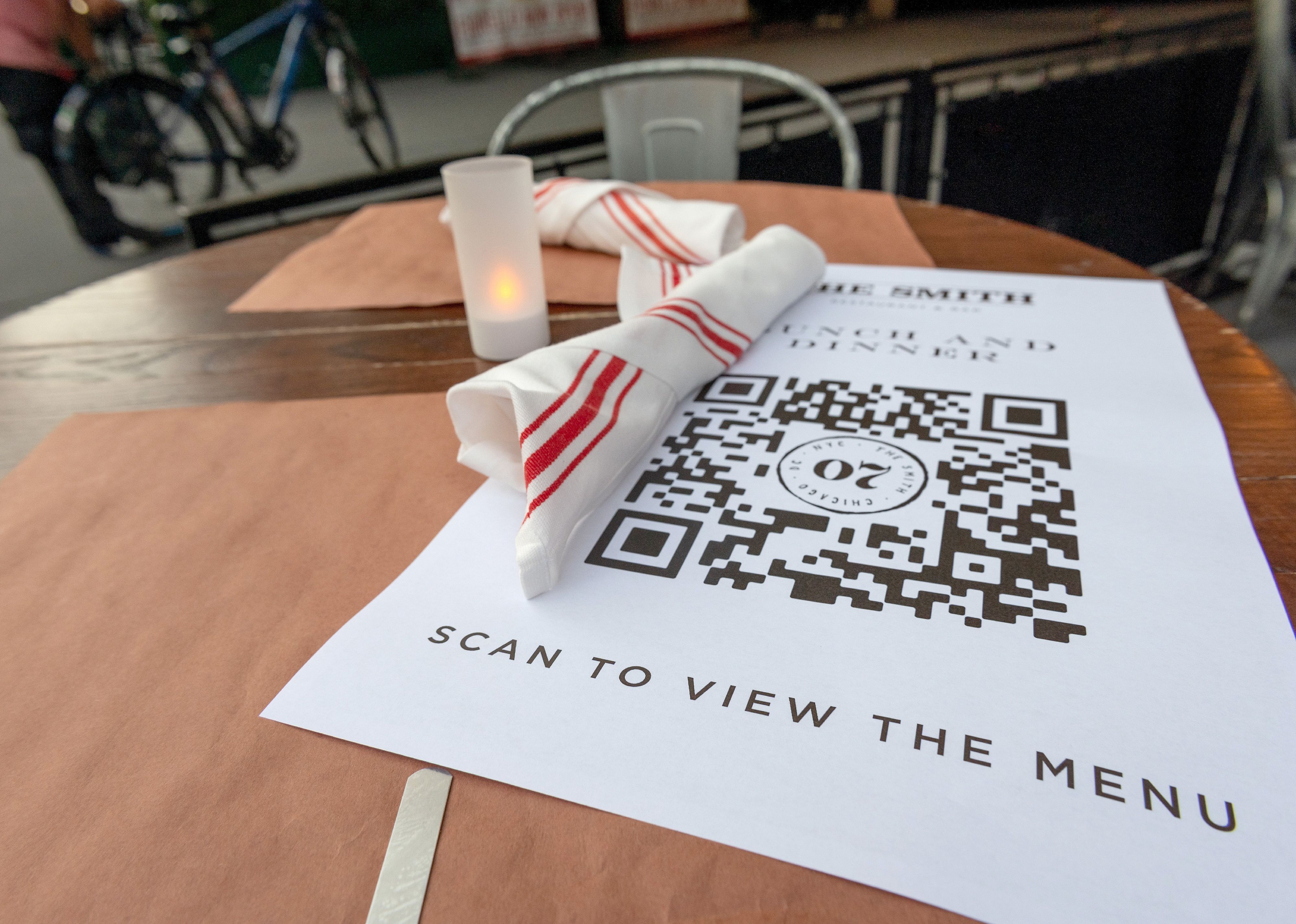 A piece of paper with a QR code and the words, scan to view the menu, sits on a restaurant table. 