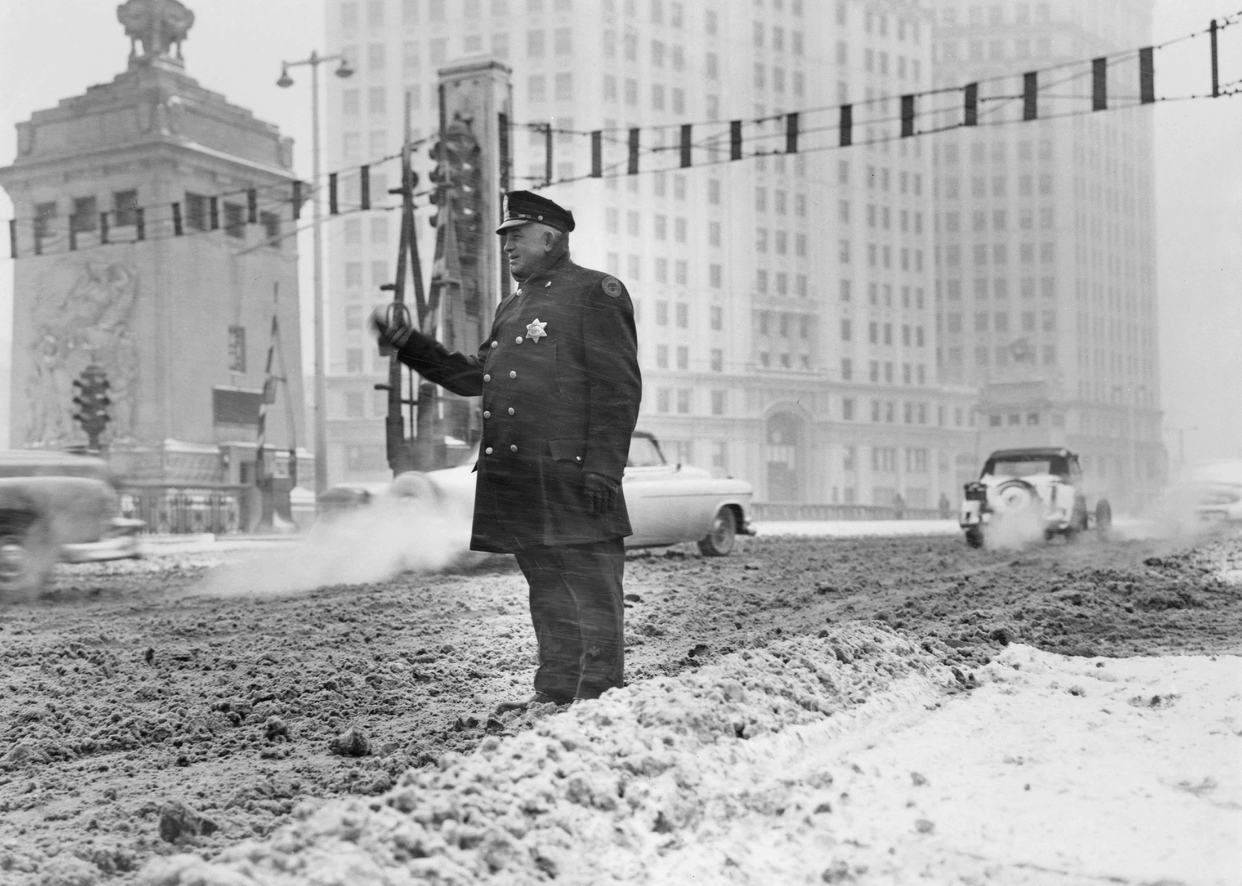 Patrolman standing in deep snow and motions 'drive slowly' warnings to motorists