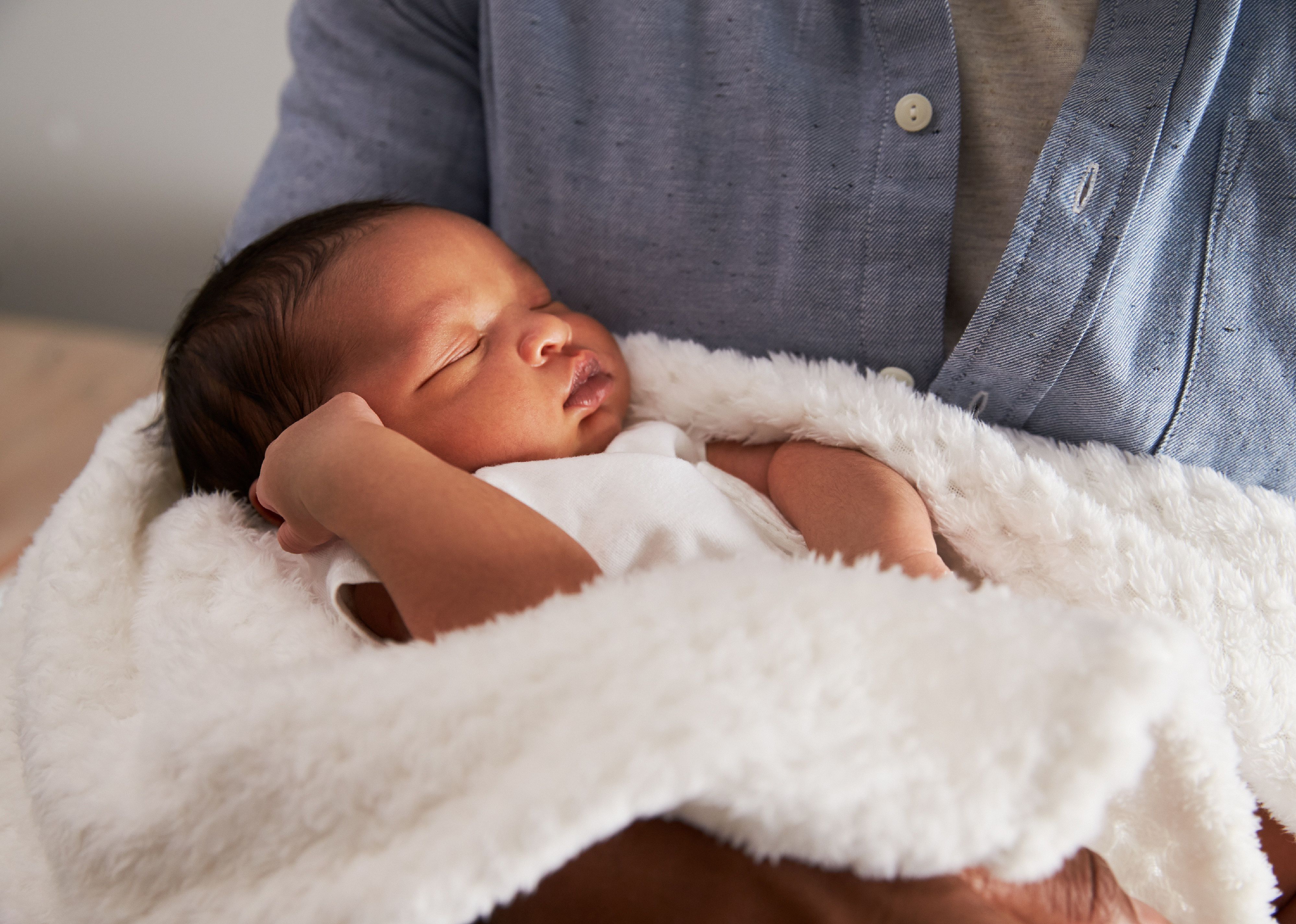 Man holding sleeping baby in white blanket.
