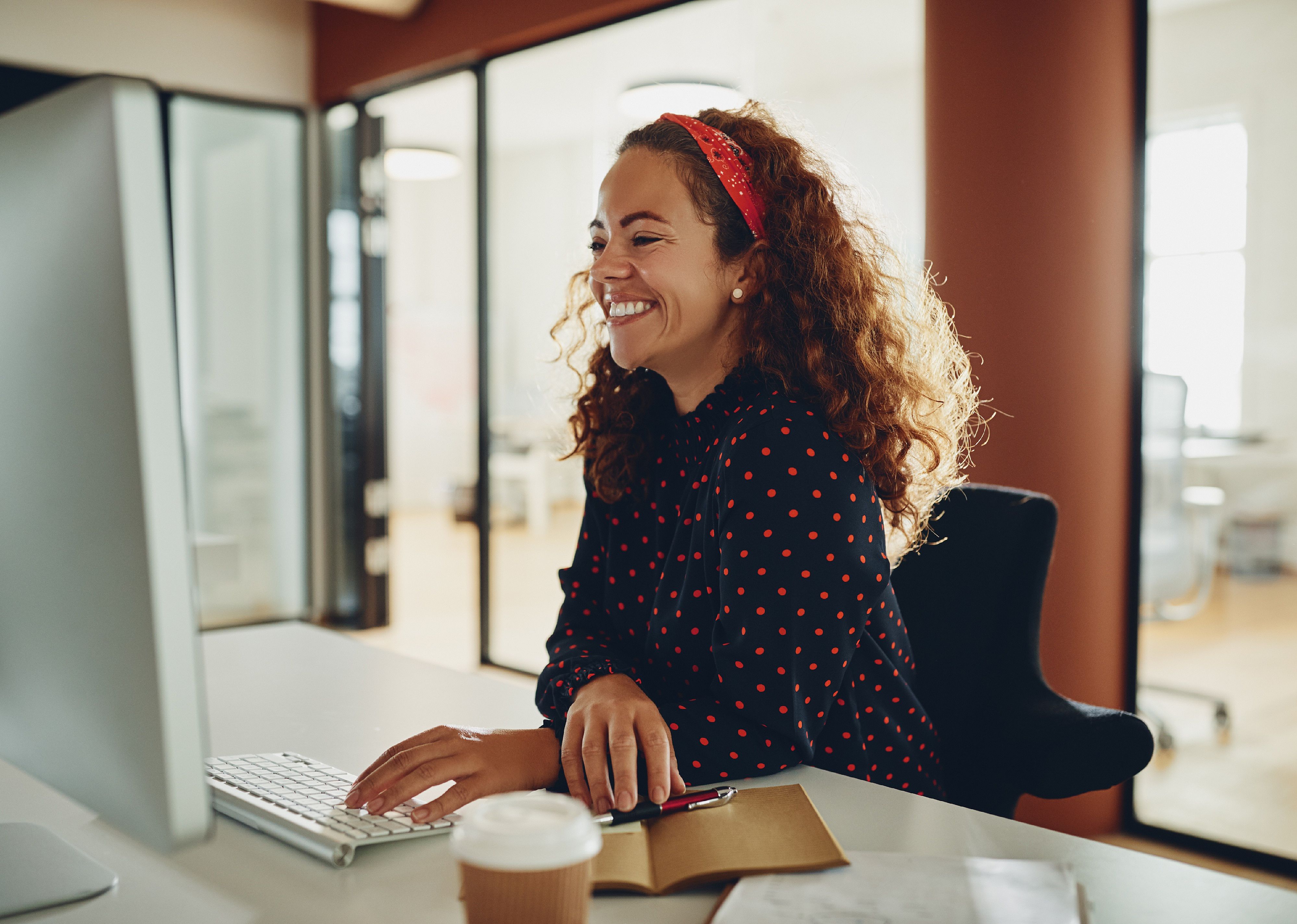 Young sitting at a desk and laughingwhile working on a computer.