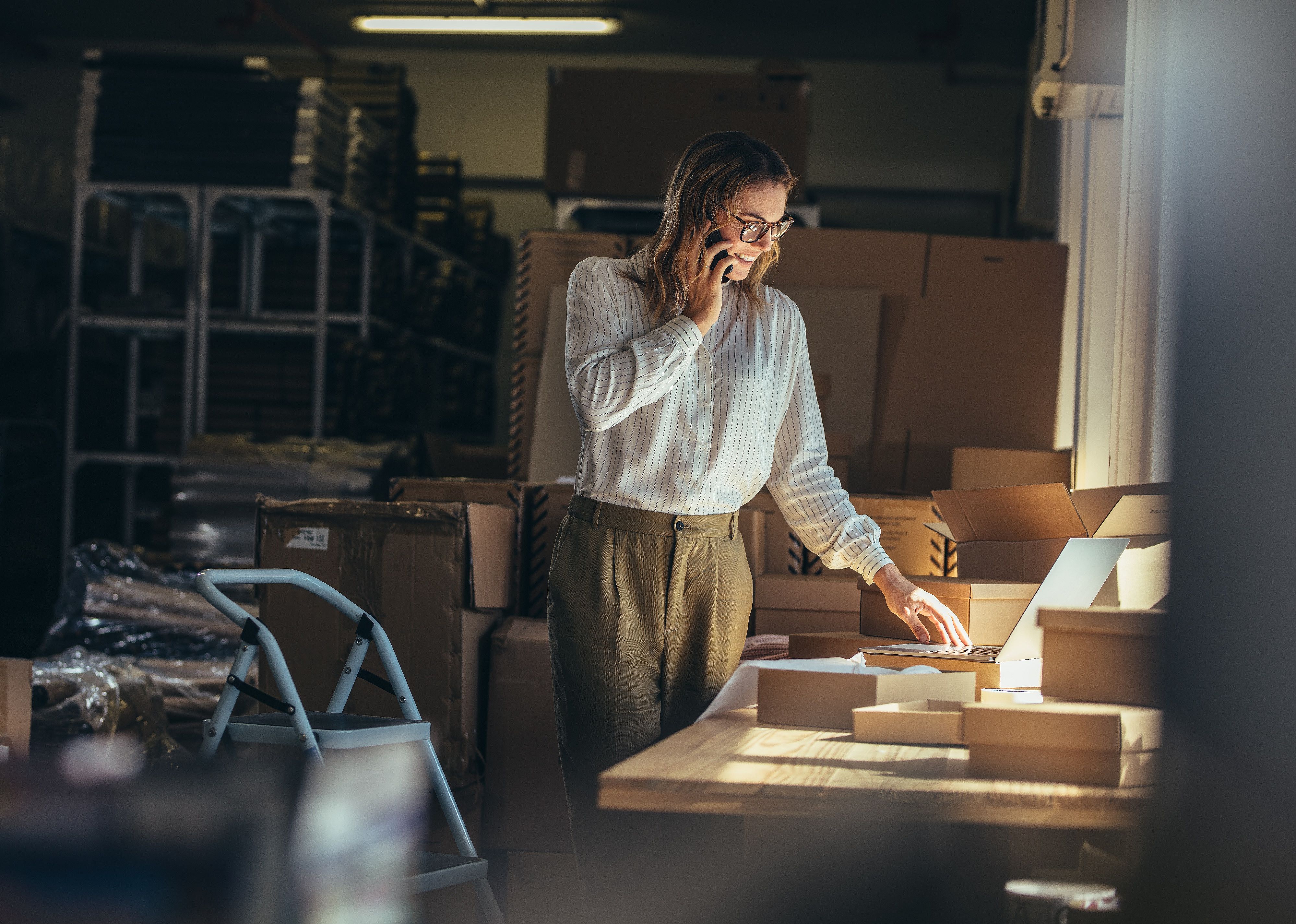 Saleswoman on the phone in a warehouse with a laptop open.