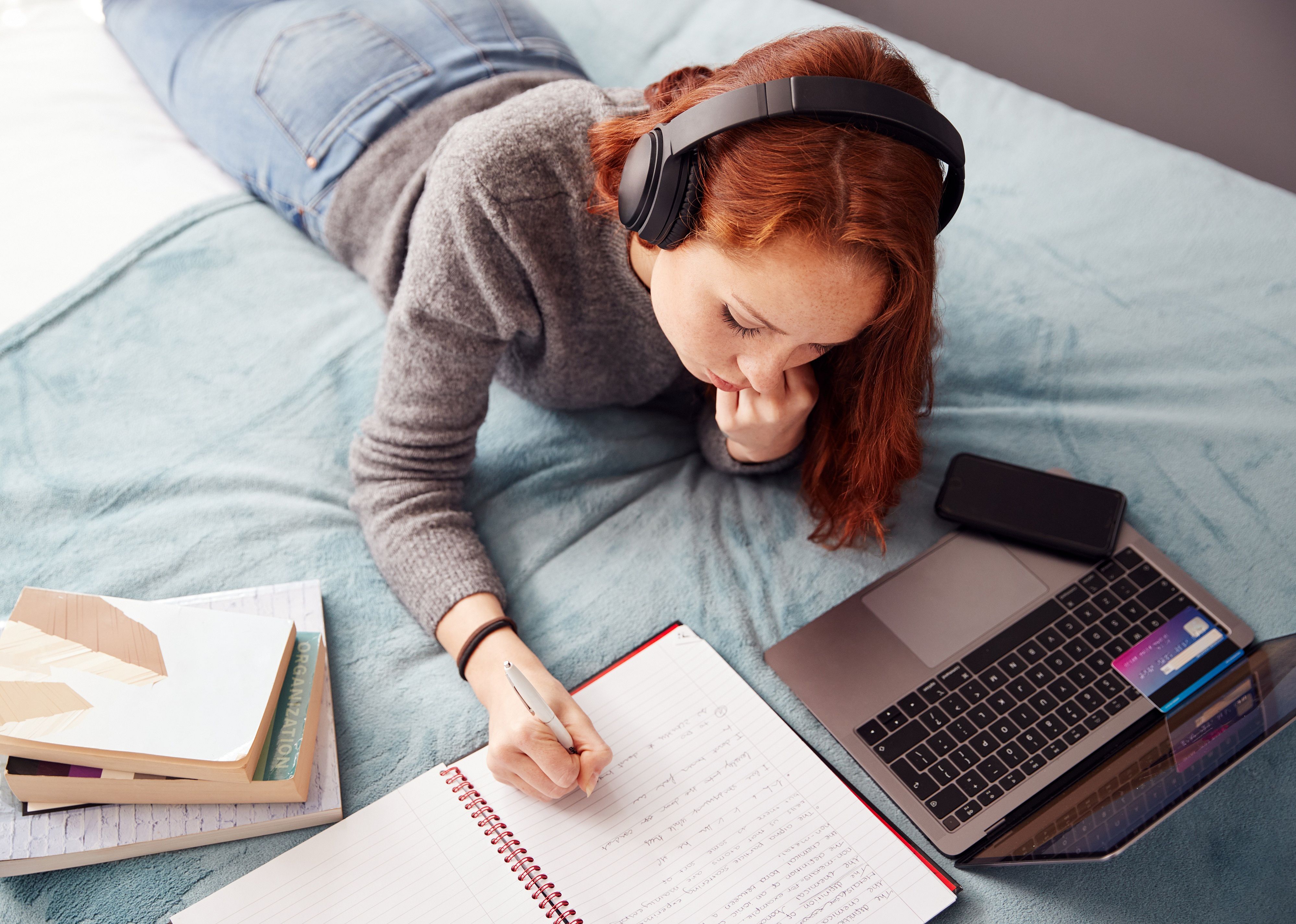 Female student on bed working on schoolwork.