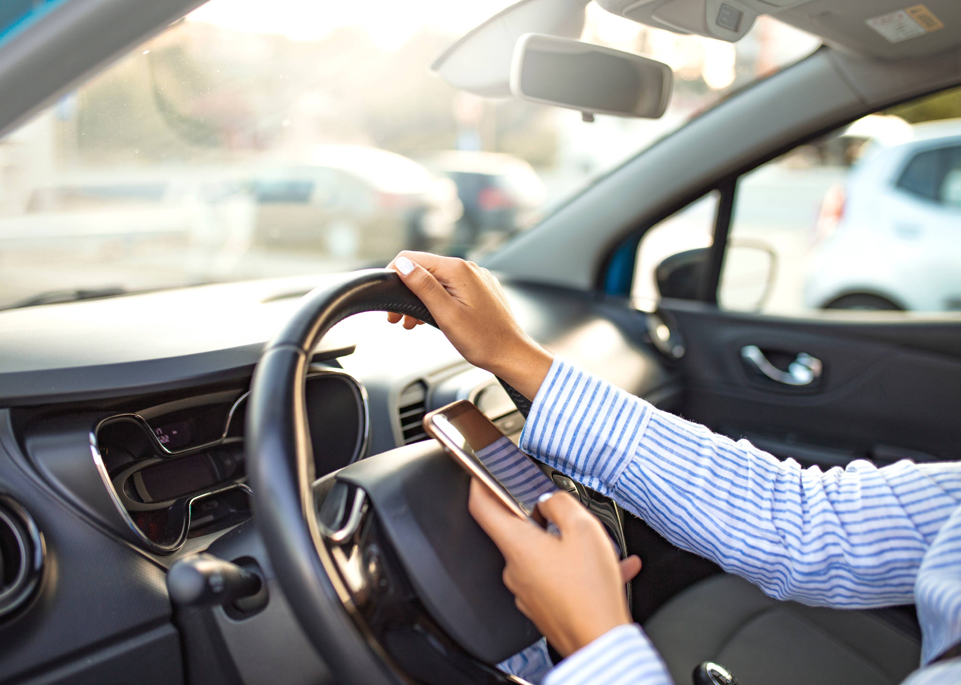 Person using phone while driving behind the wheel.