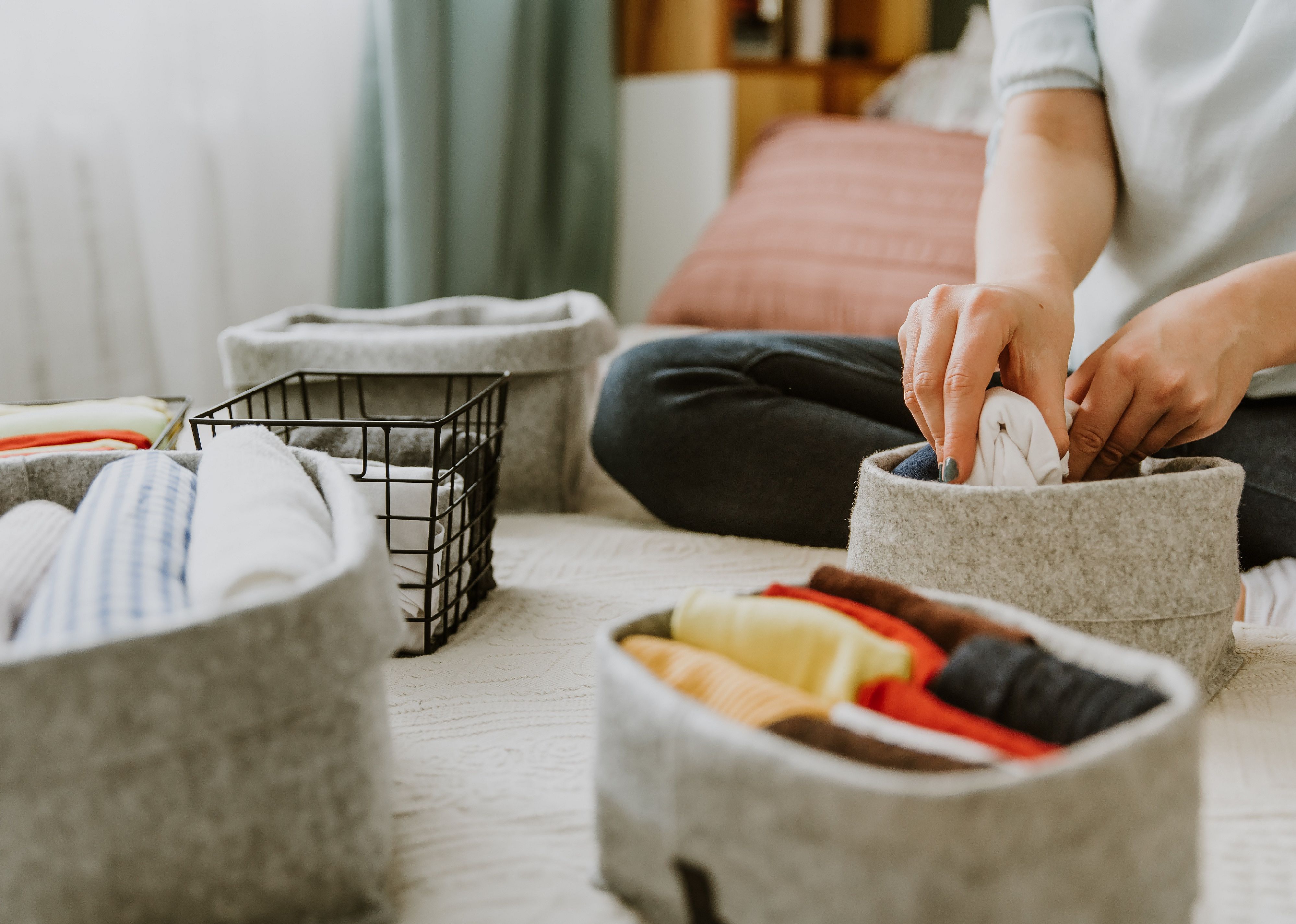 A person folds clothes into fabric storage bins.