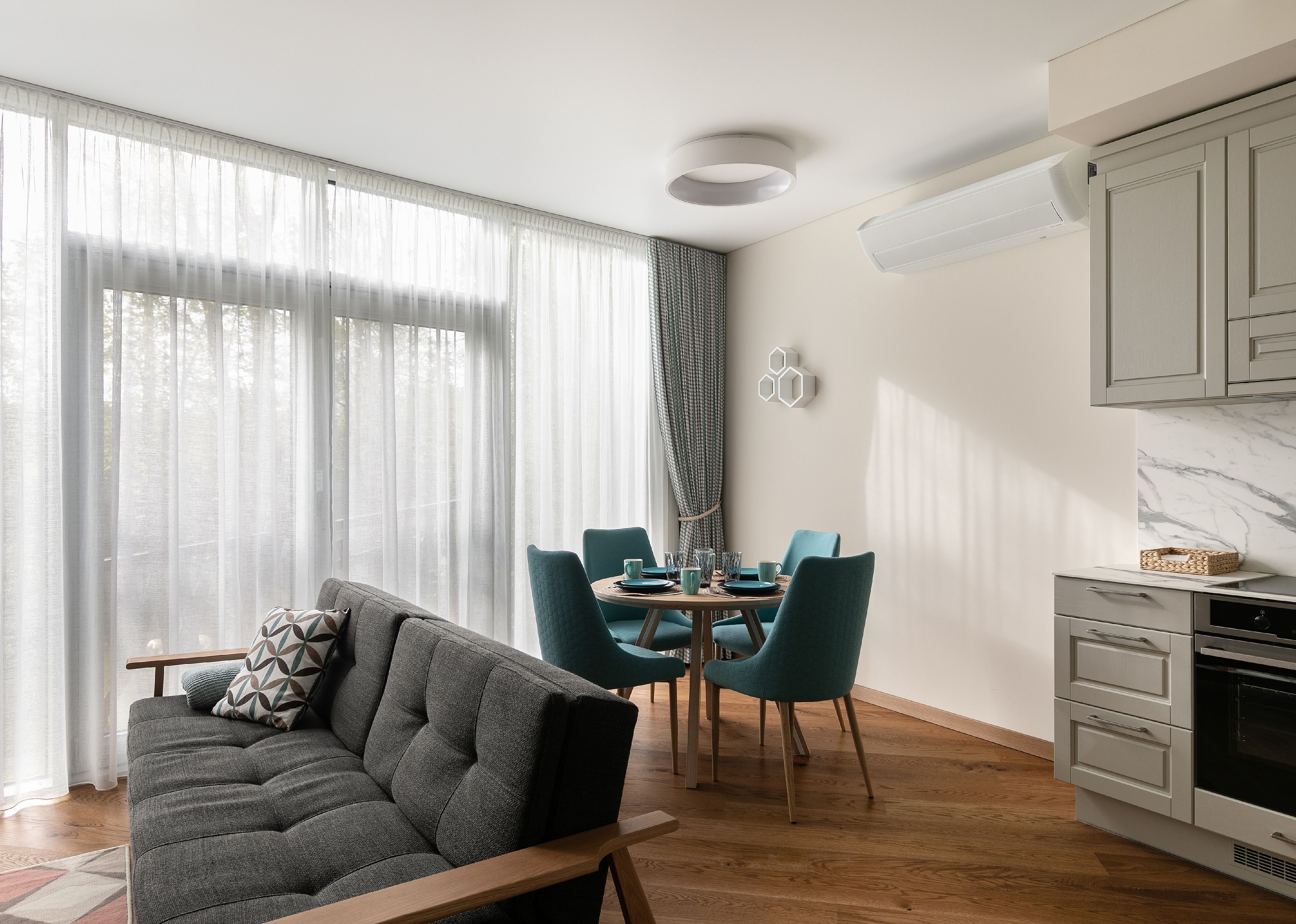 Living room in a small apartment furnished with gray sofa, round table and blue chairs.