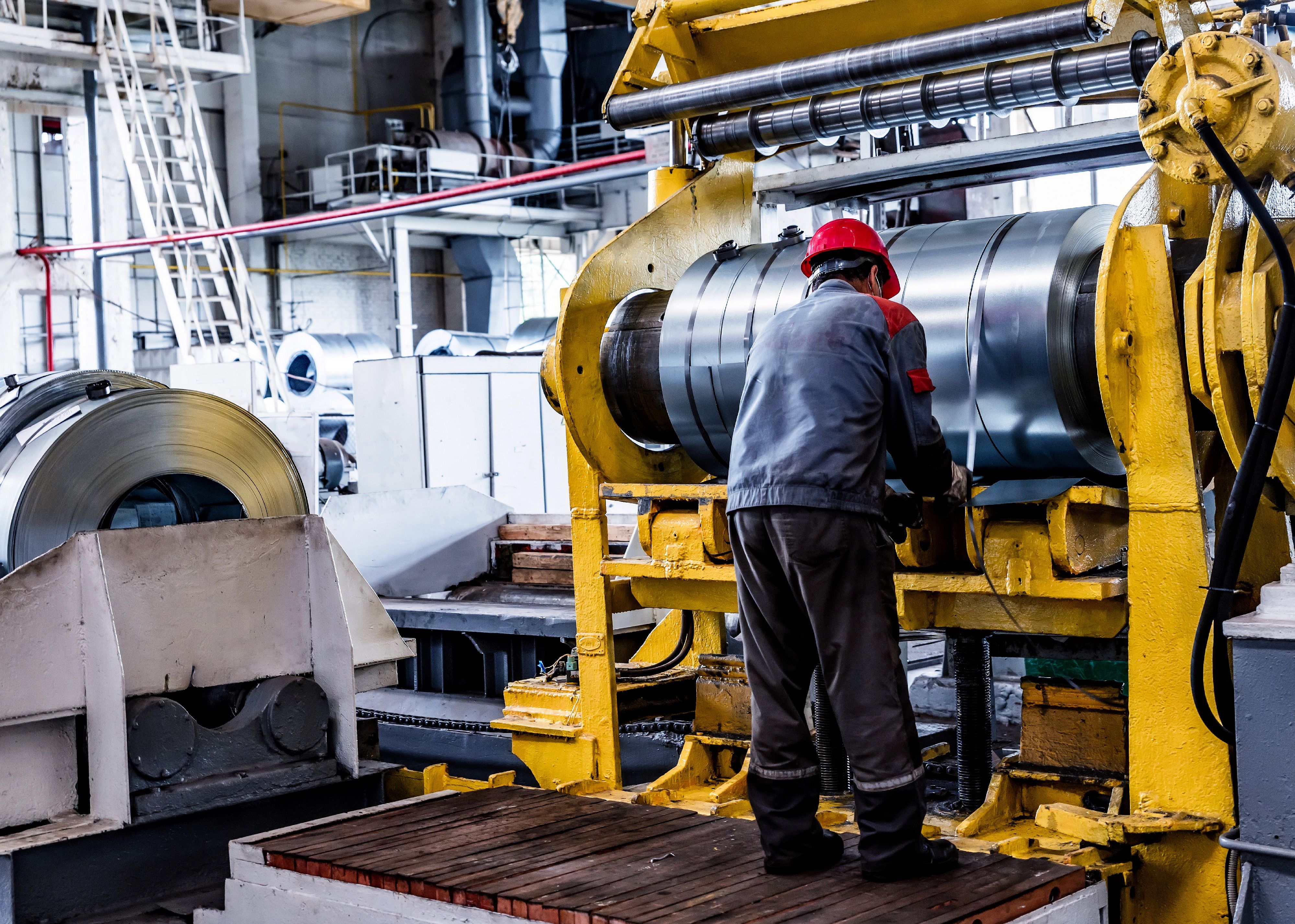 Worker and stock with rolls of sheet steel in industrial plant.