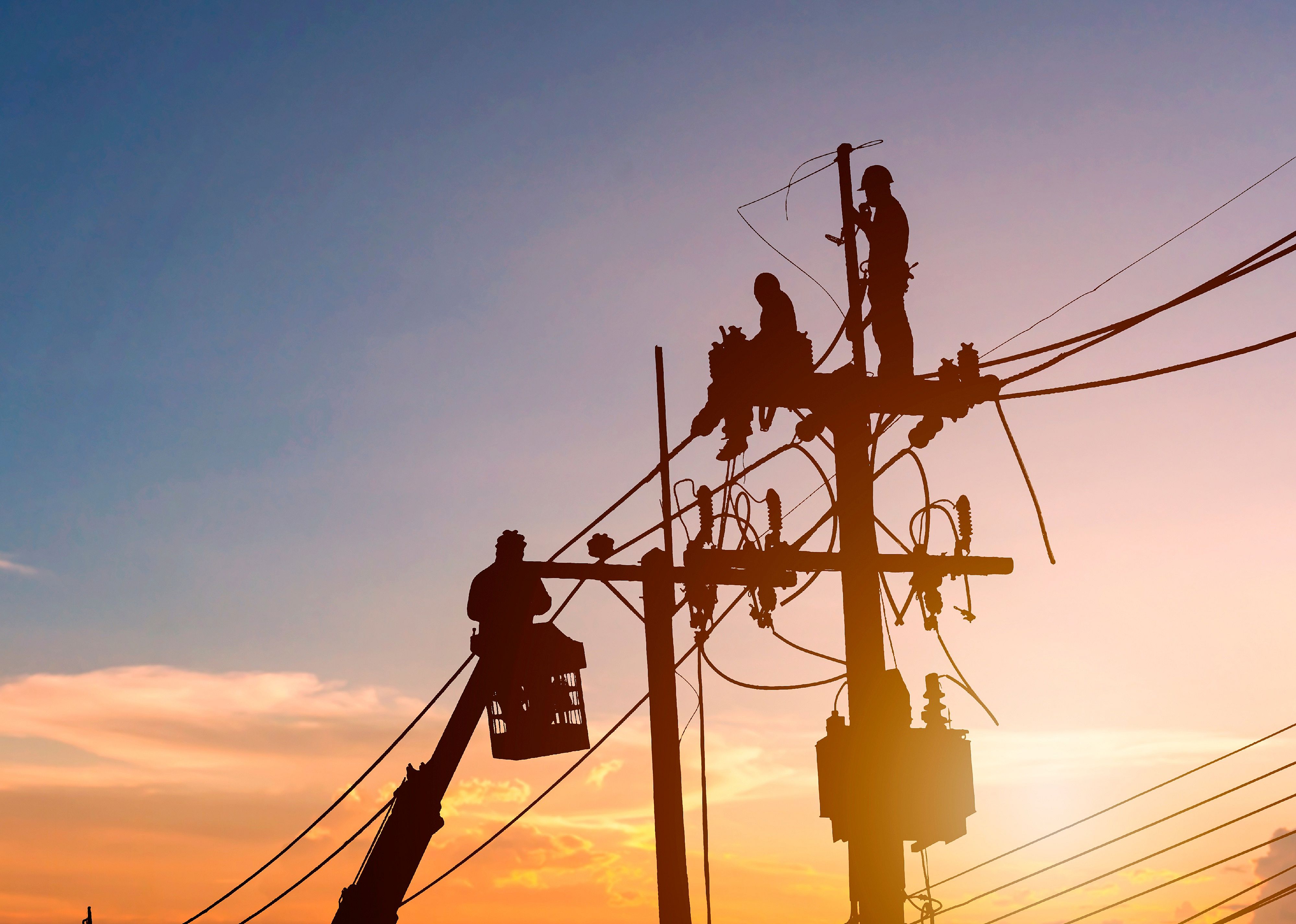 Silhouetted electrician working on poles to install high-voltage equipment.