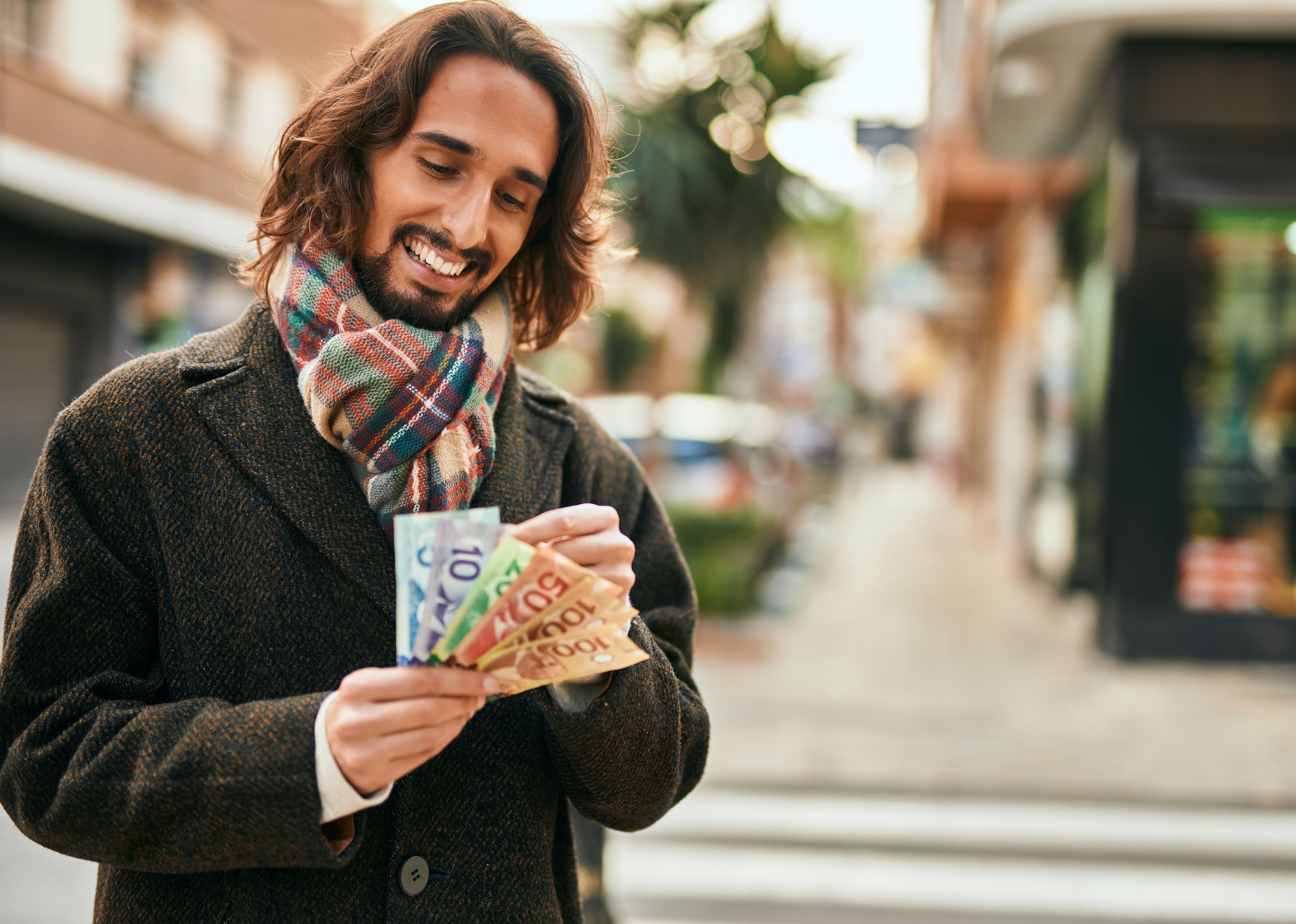 Young man smiling counting Canadian dollars in a city.