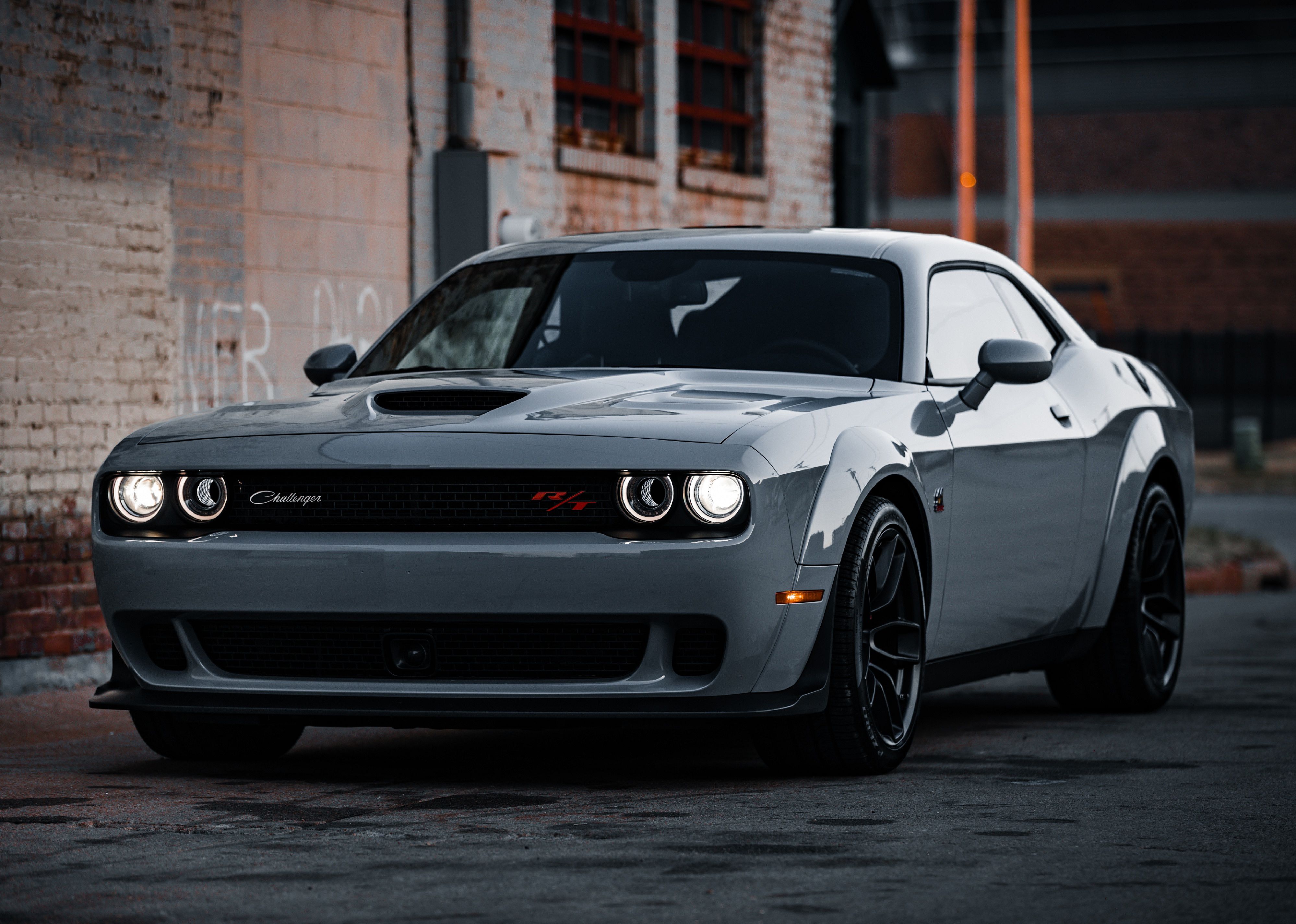 A green-gray Dodge Challenger outside by brick building.