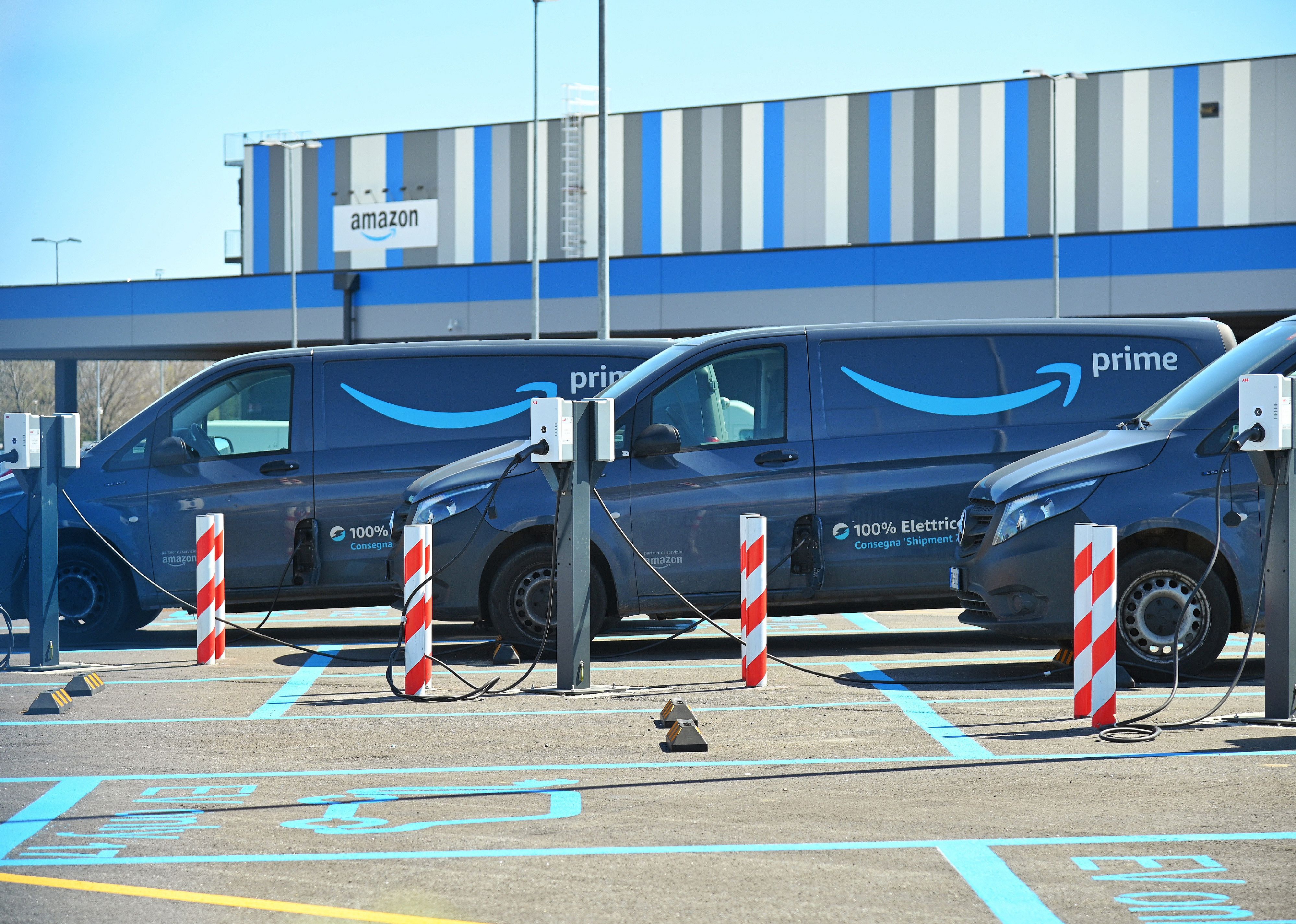 Row of electric Amazon delivery vans parked and plugged in at a logistic hub