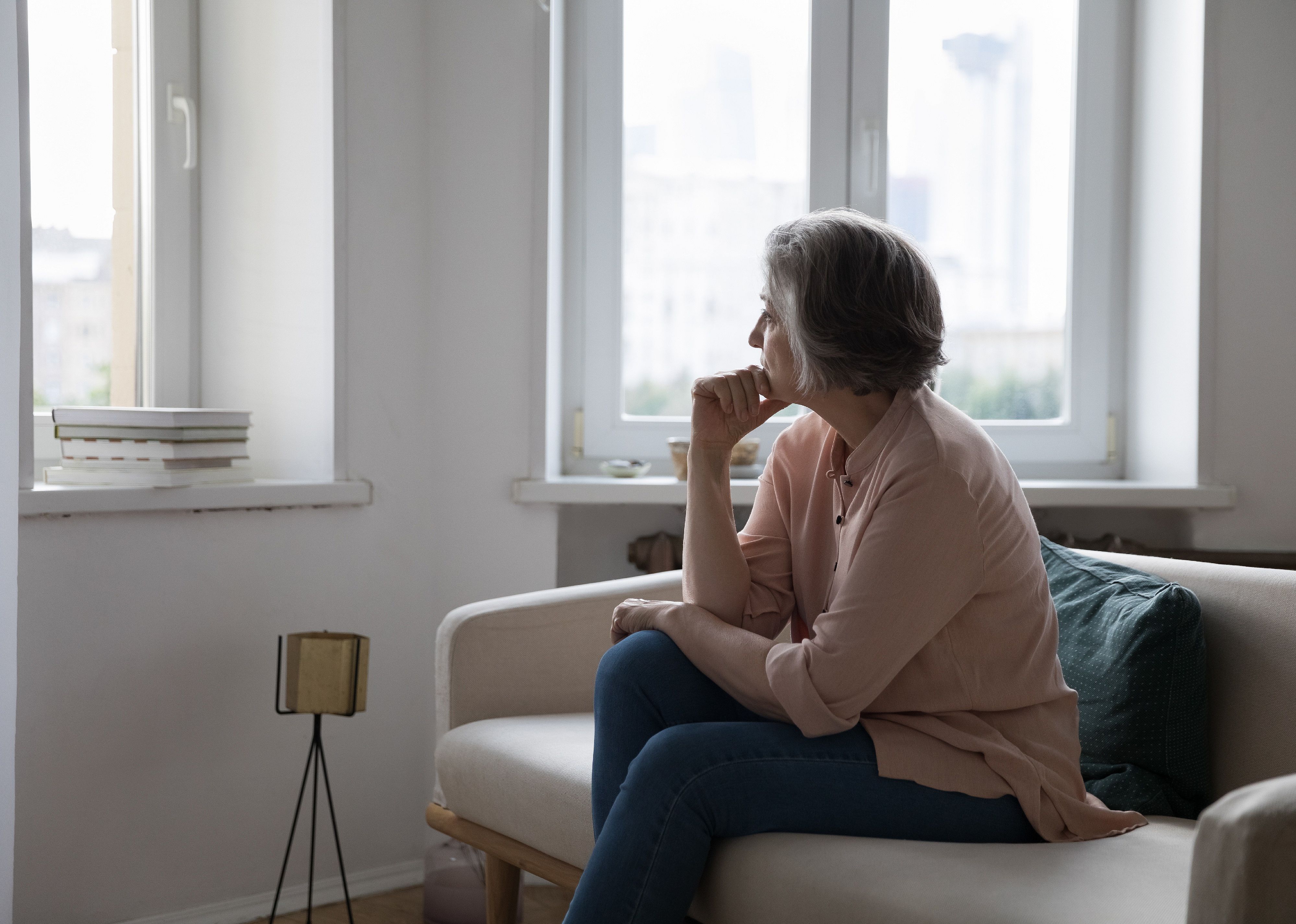 Mature lady looking out window, looking sad.