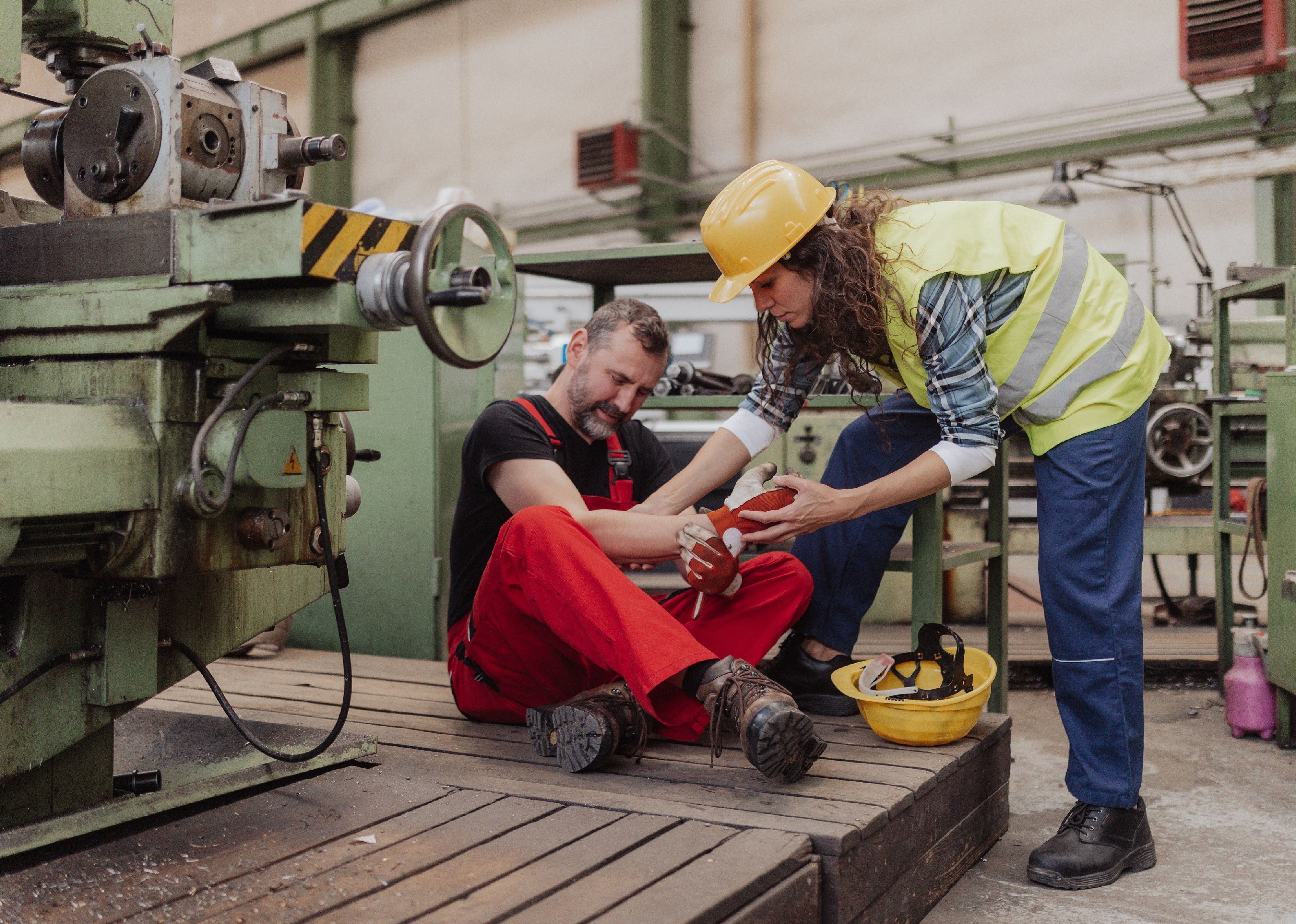 Woman is helping her colleague after accident in factory.