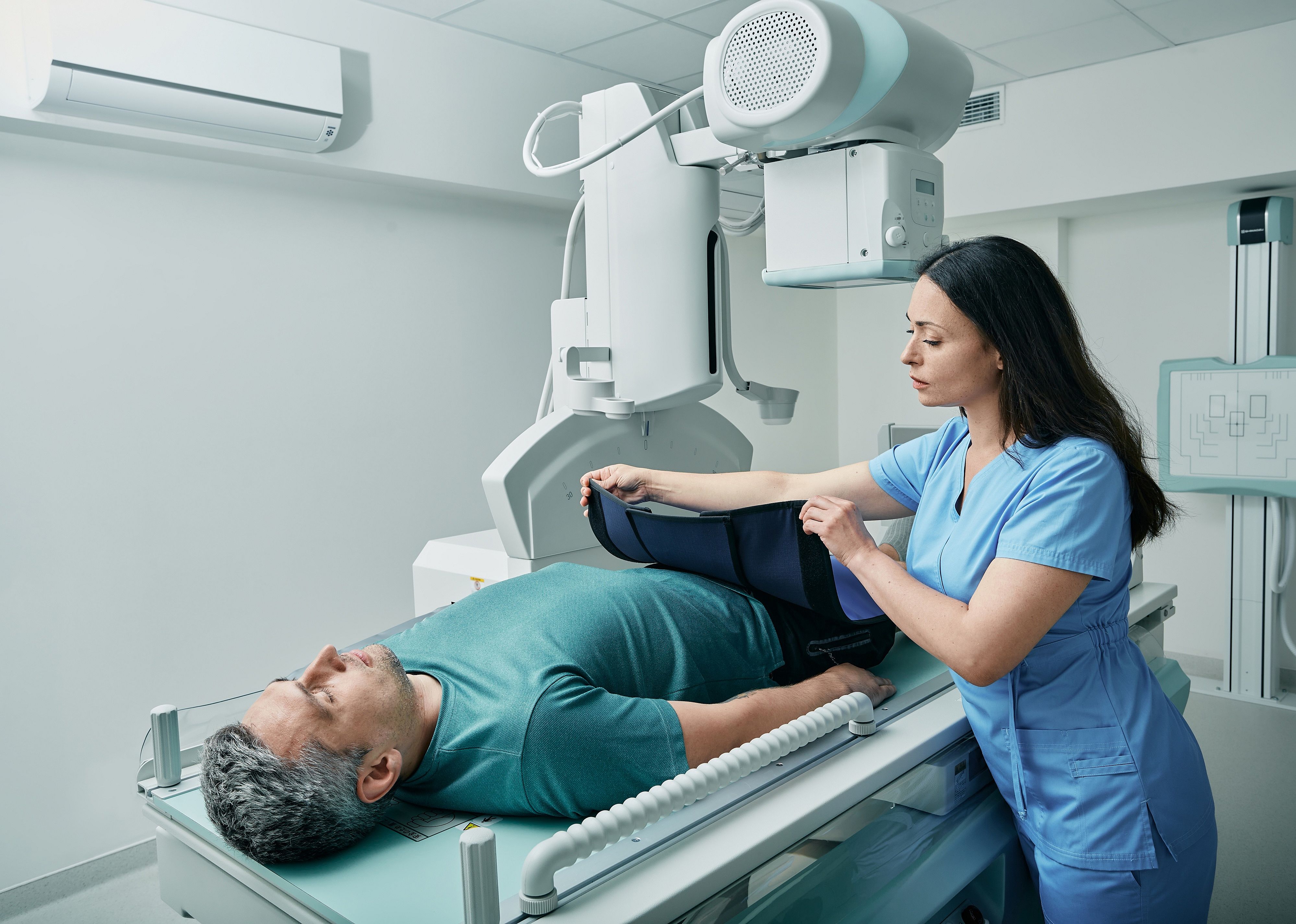 Technician preparing patient for a X-ray in radiographic imaging room.