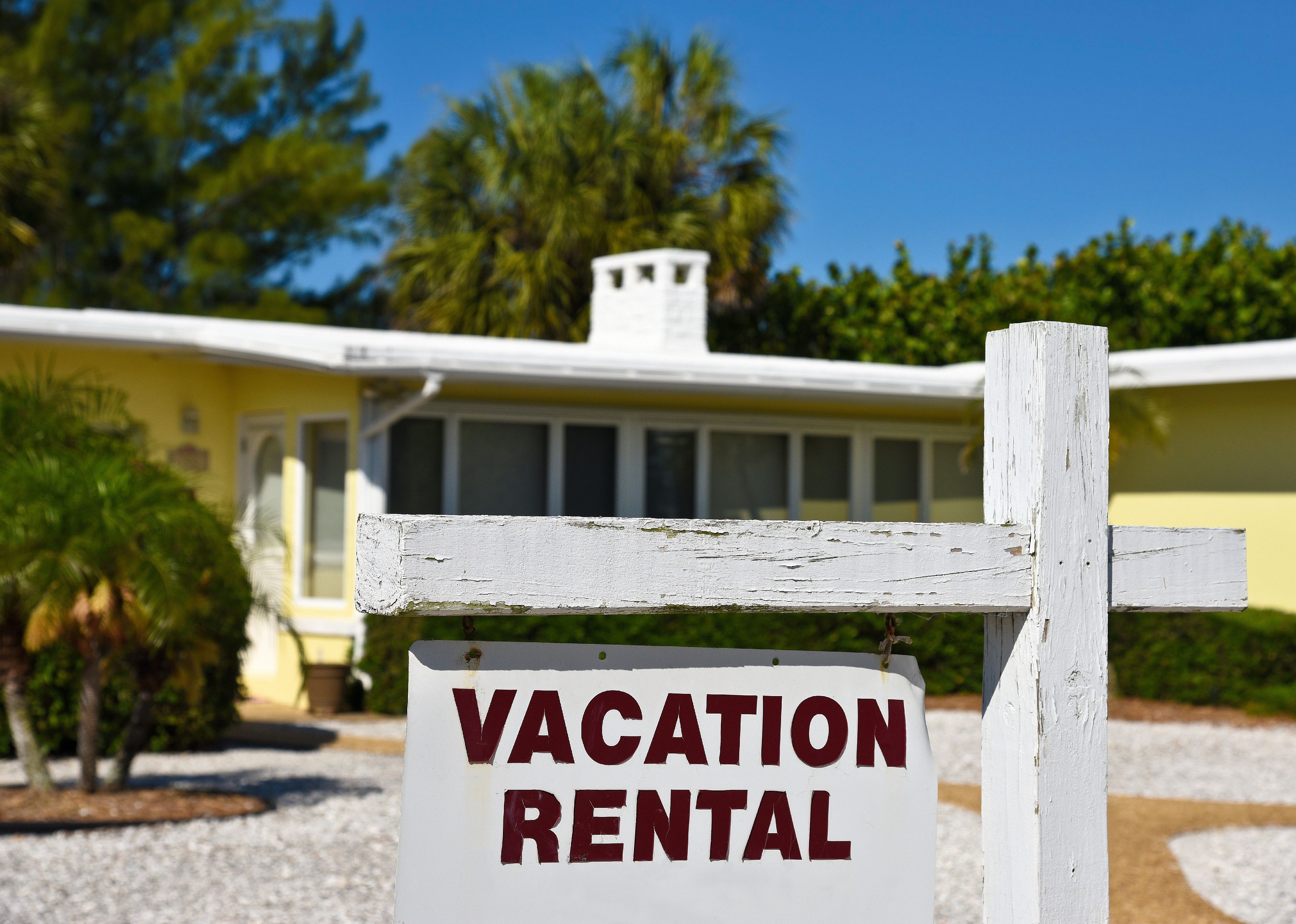 A Vacation Rental Sign in front of a yellow one story home on the beach.