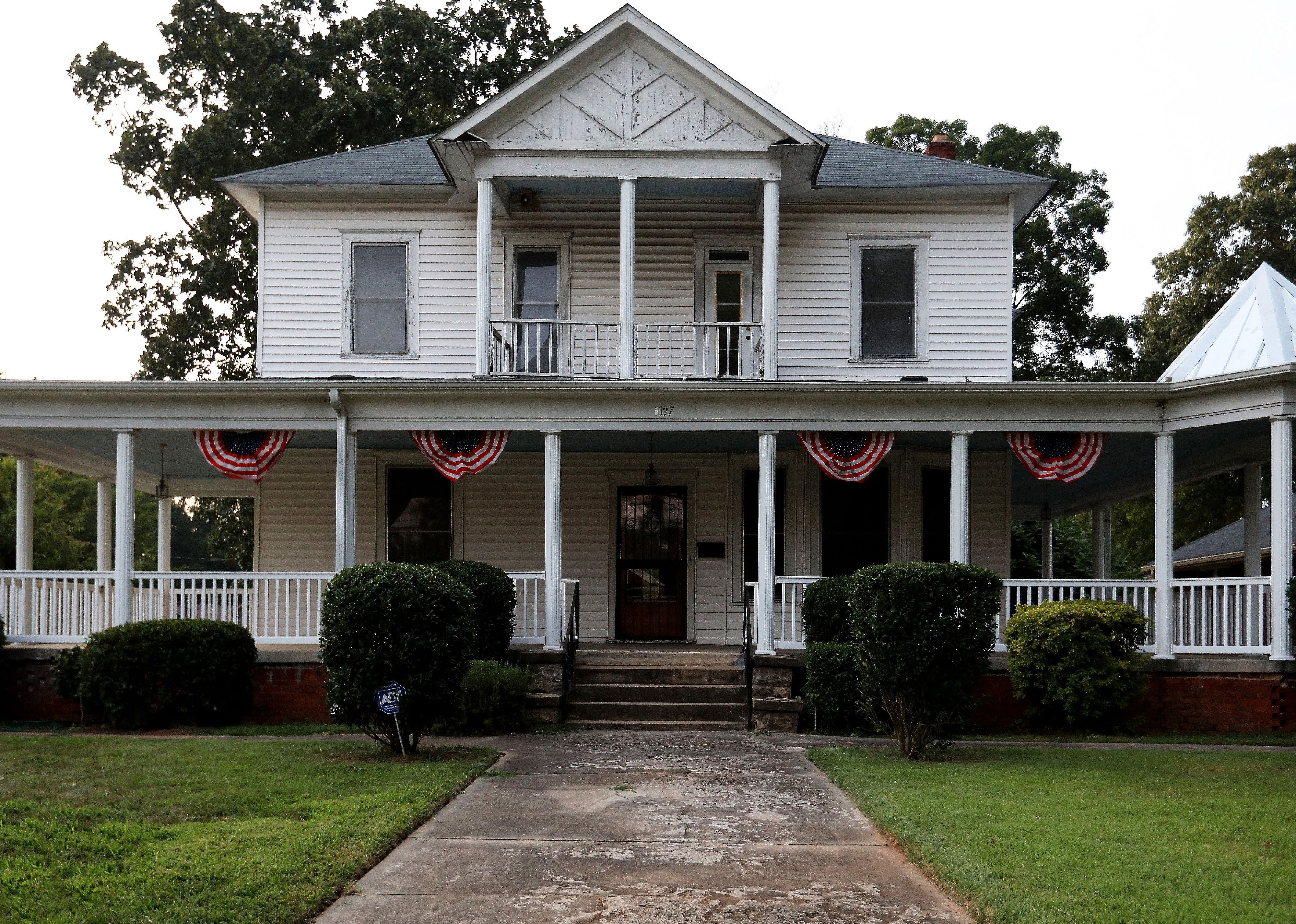 A two story white house with a wrap around porch.