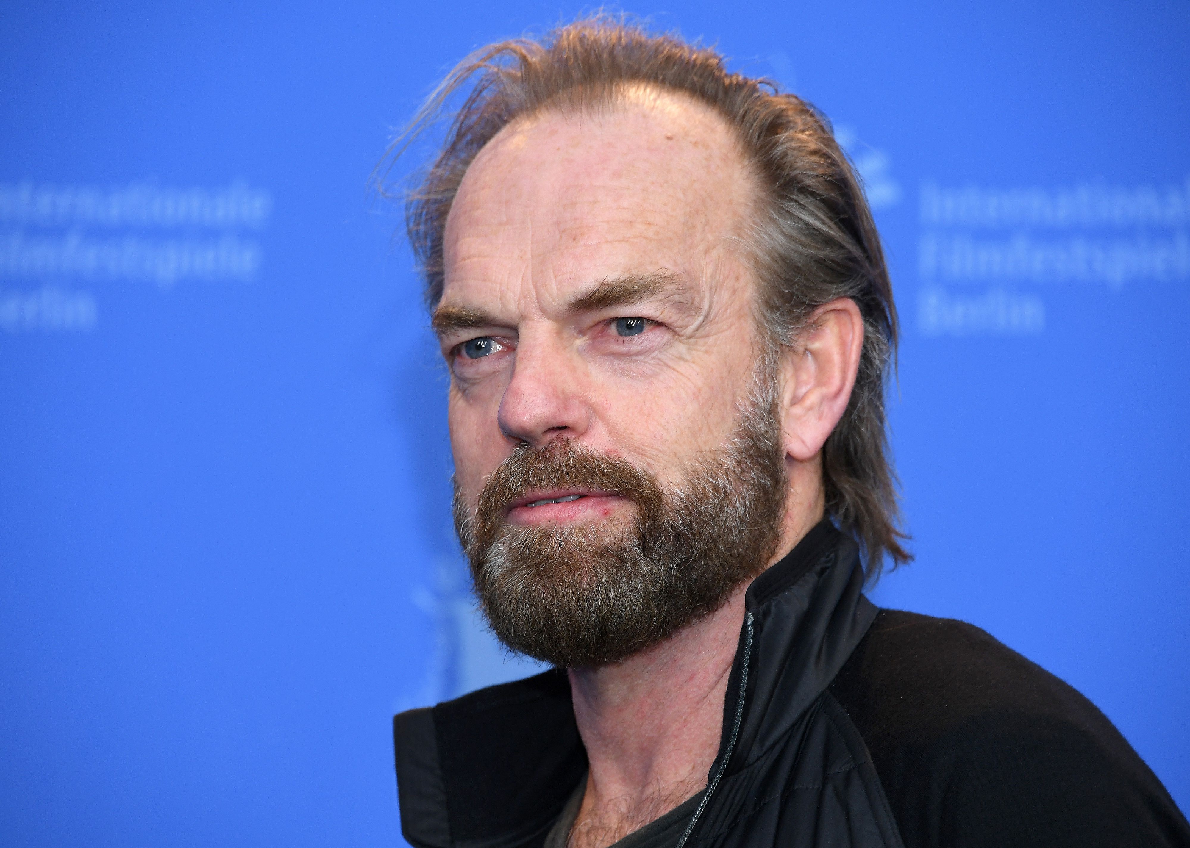 Hugo Weaving in black against a blue background.