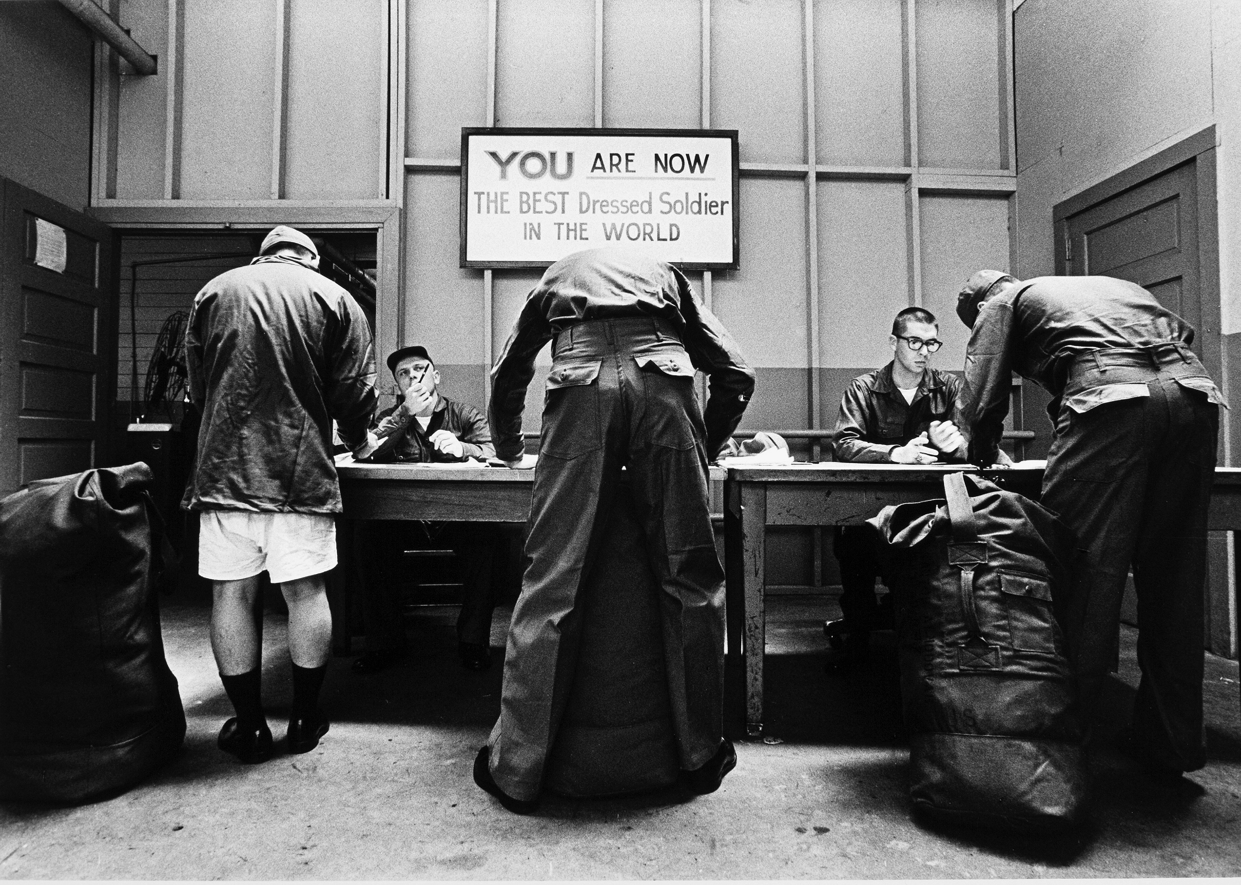 Three recently drafted soldiers sign papers under a sign that reads 'You are the Best Dressed Solider in the World' at Fort Jackson.