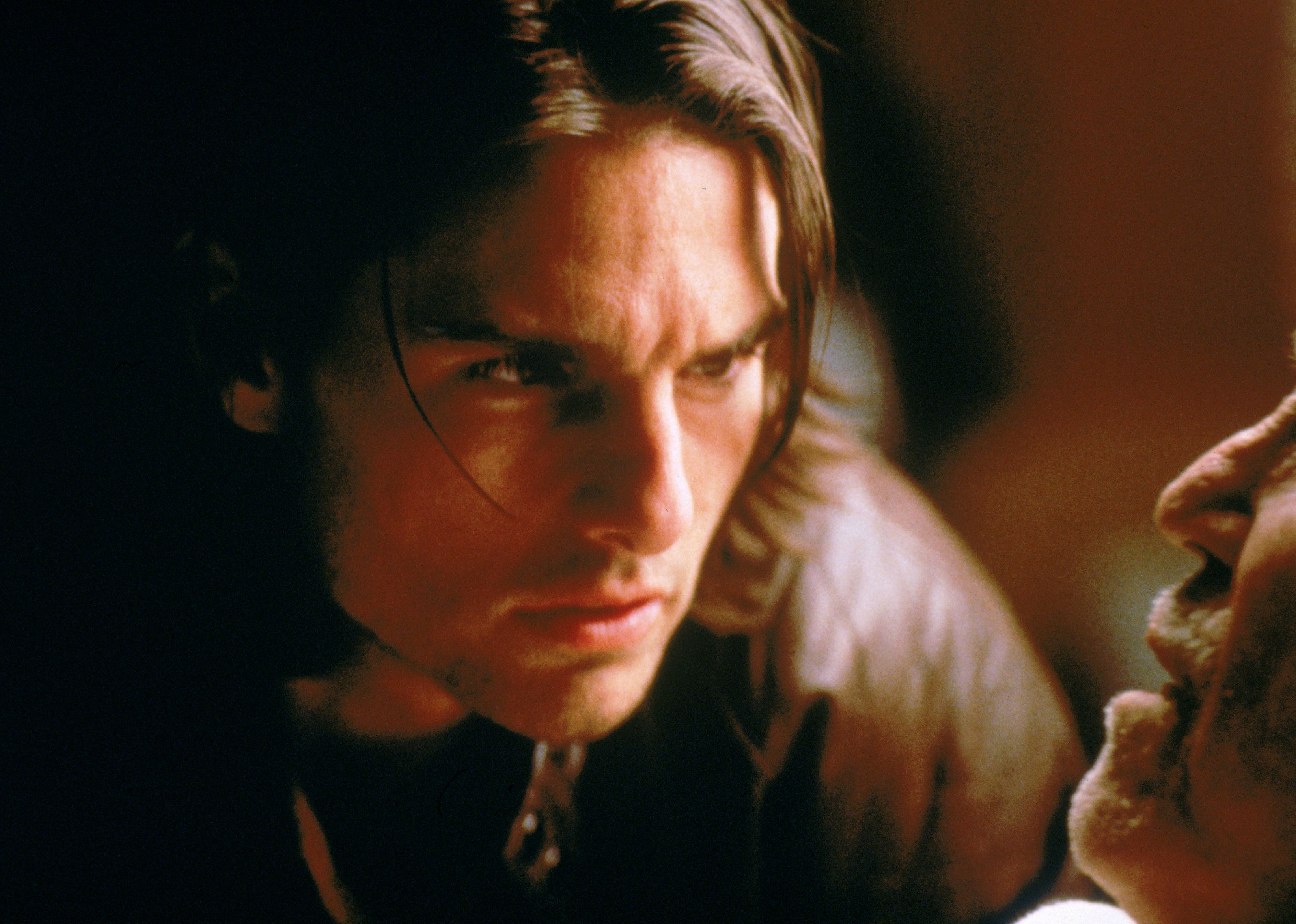 Tom Cruise, with long hair, leans in to listen to a man who looks ill.