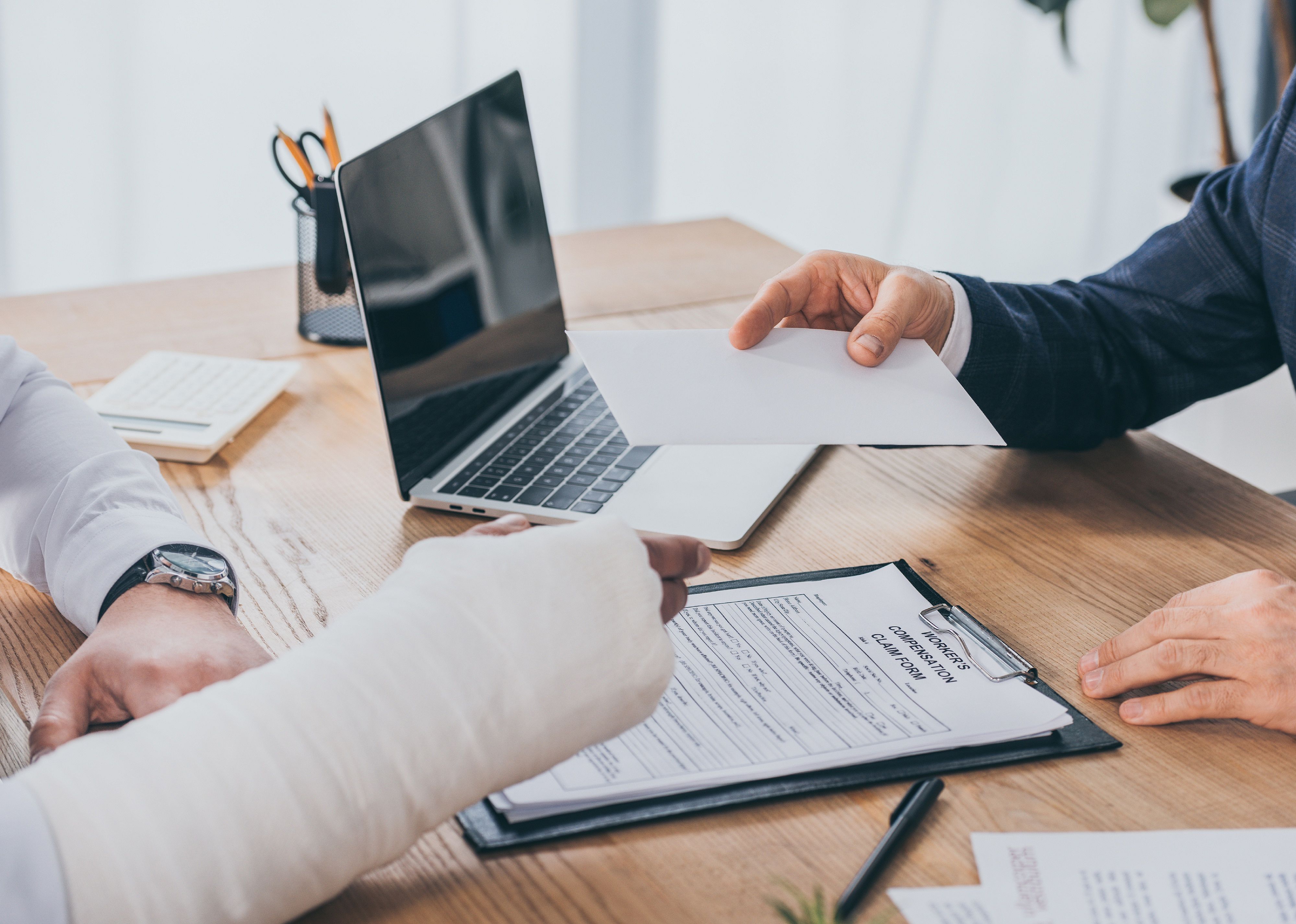 Cropped view of businessman giving paper to worker with broken arm in office.