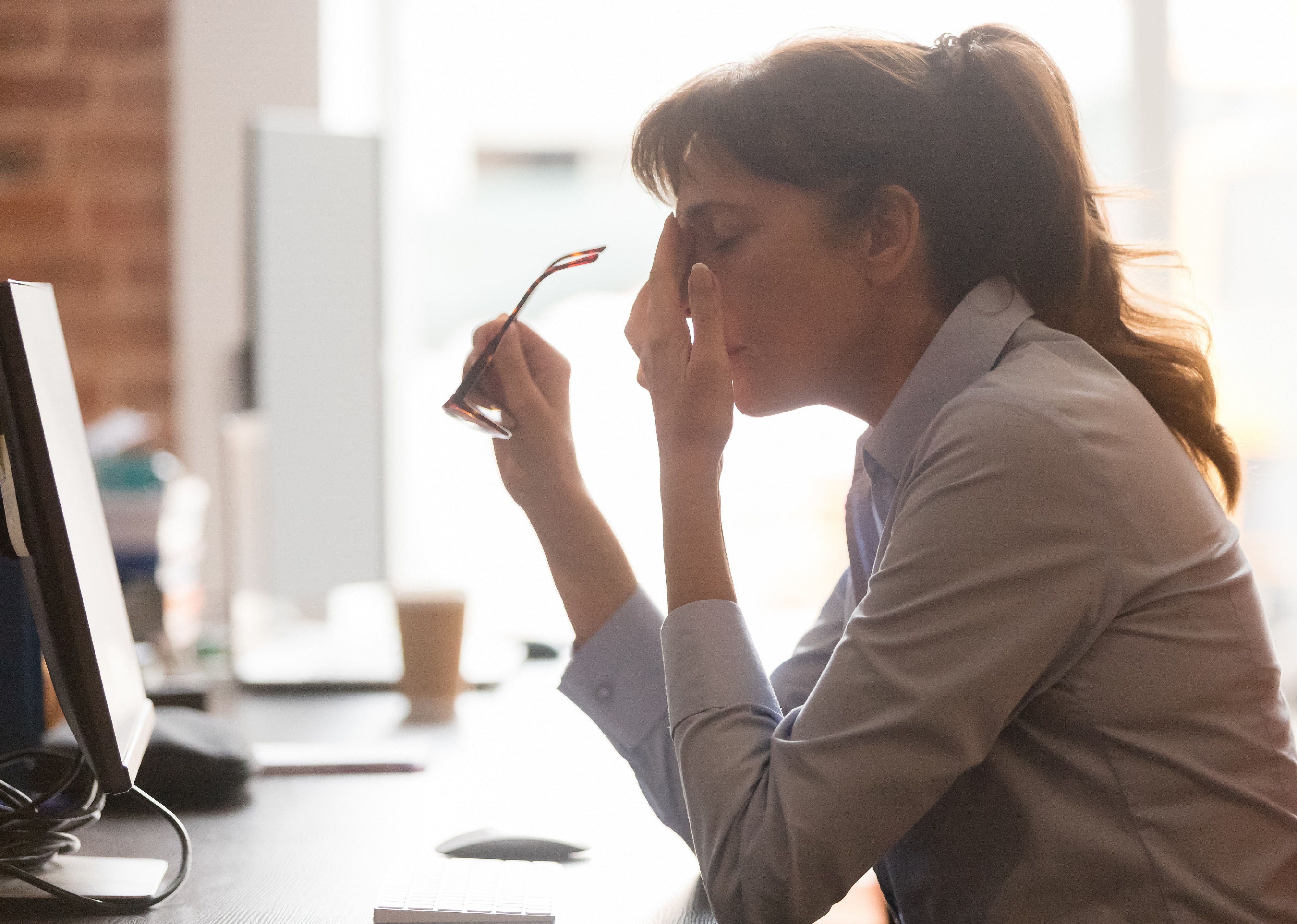 Female worker at office desk takes off glasses