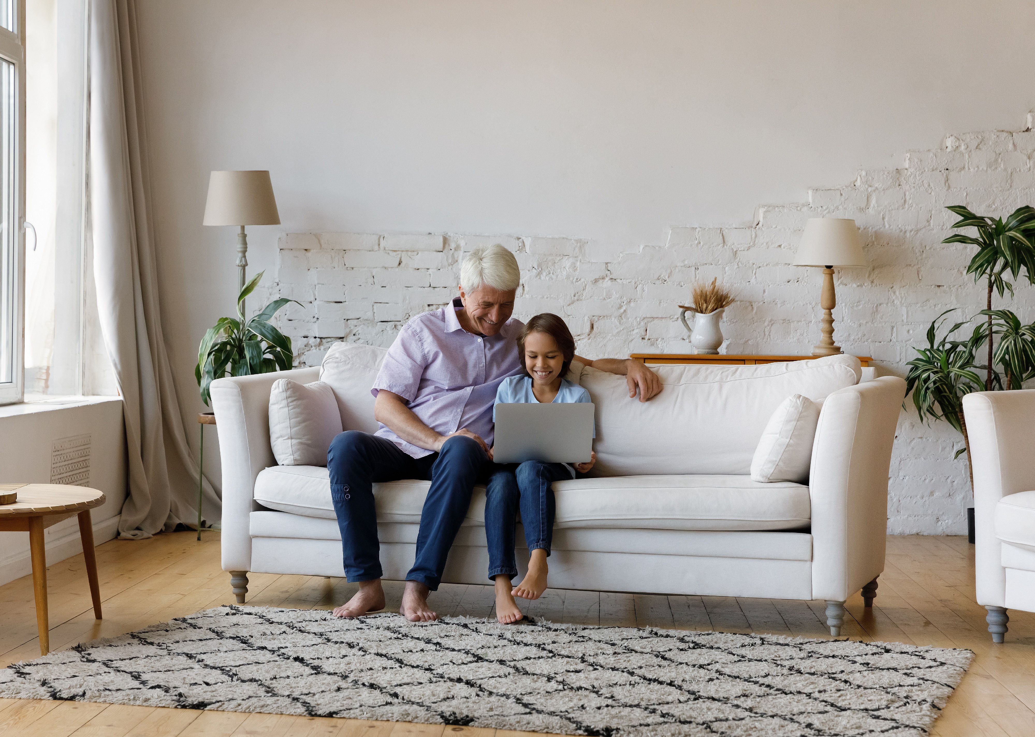 Grandpa and grandkid it on a sofa and use laptop.