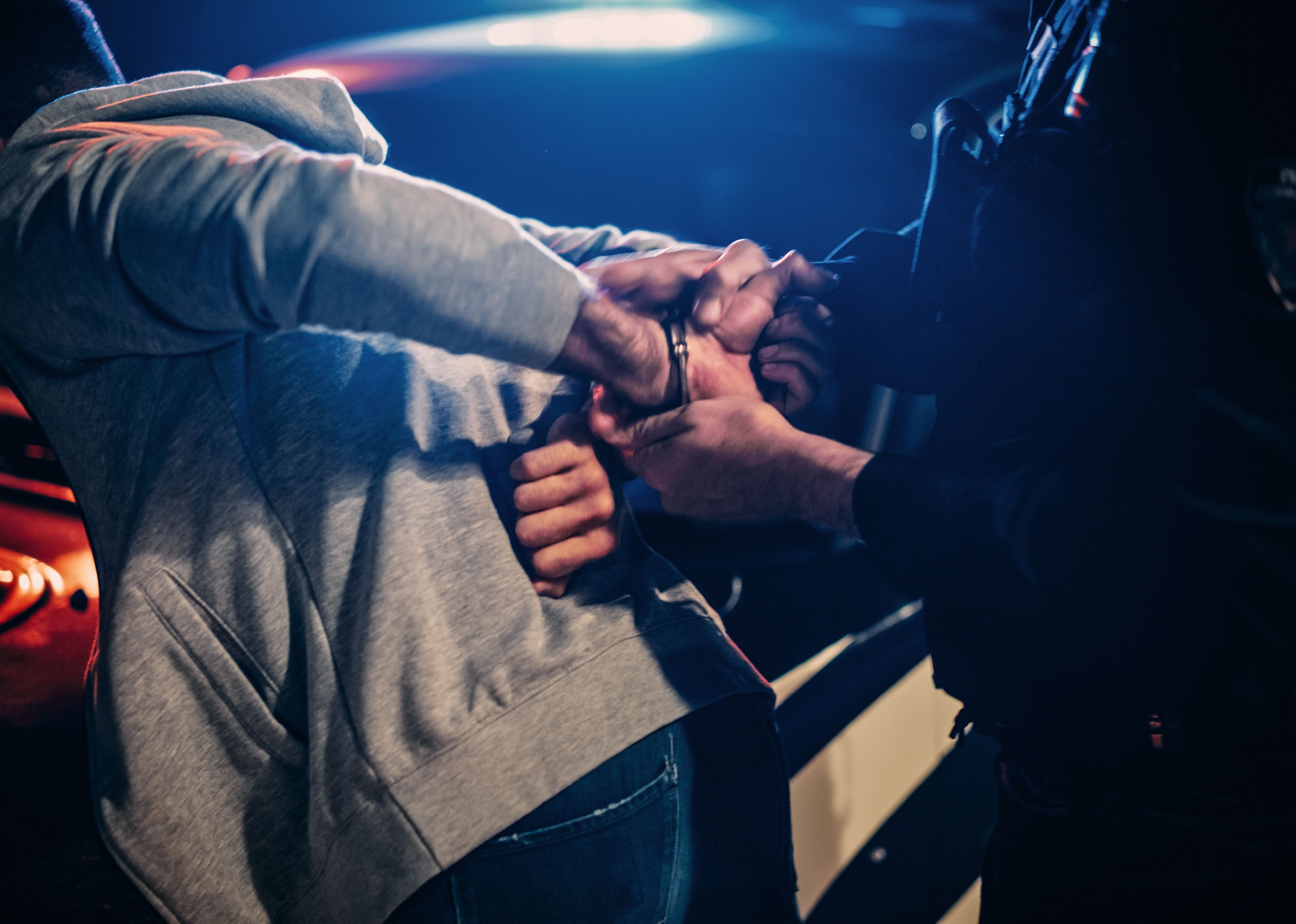 Officer pushing man against a car and handcuffing him.
