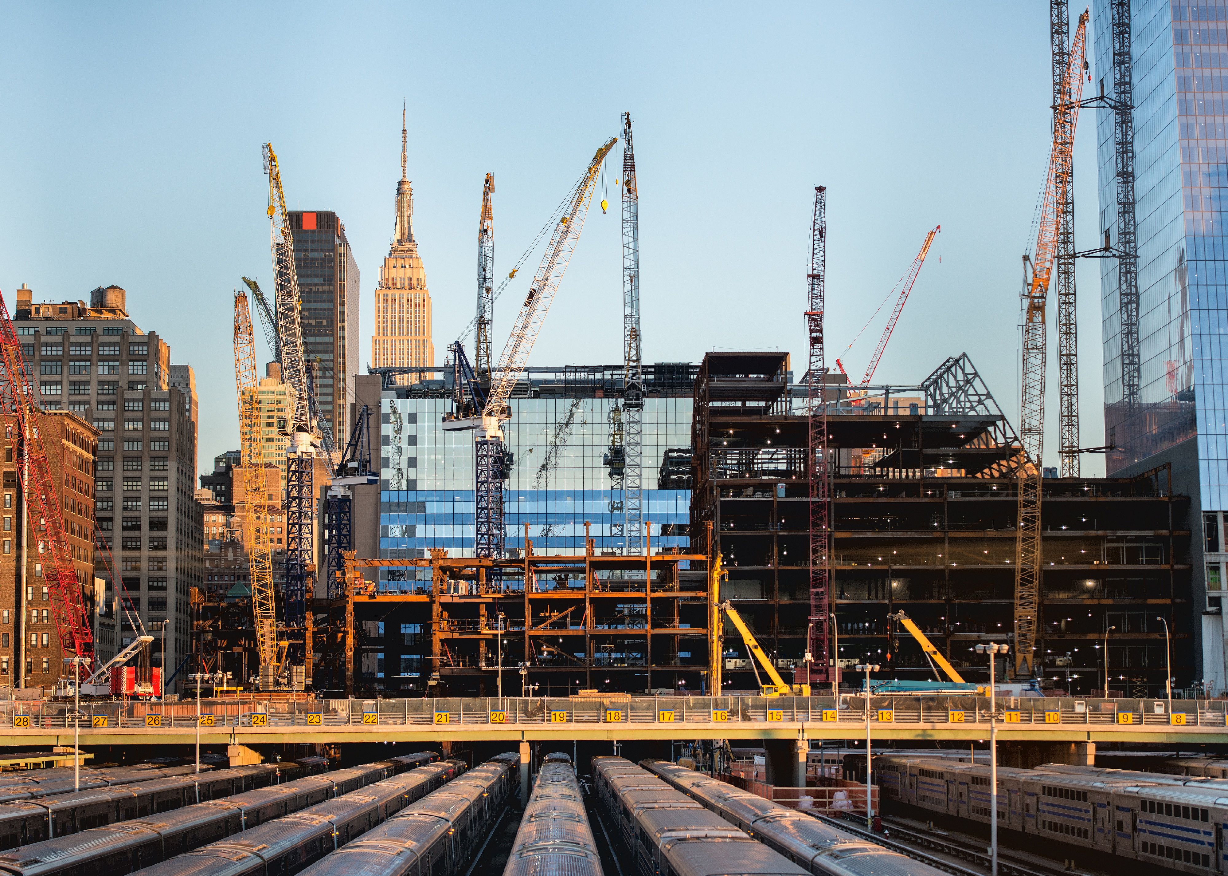 Tall buildings under construction and cranes under a blue sky in New York City.