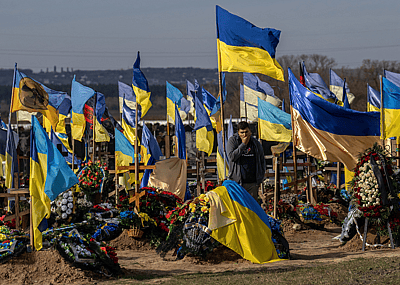 A man pauses by a grave as Ukrainian flags fly in a cemetery for soldiers killed in action.