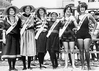 Six women pose wearing different swimsuits, with each wearing a sash that says "Miss" and the year the swimsuit was popular, including 1897, 1904, 1910, 1920, 1927, and tomorrow.