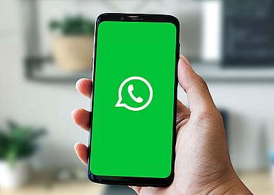 Hand holding a smartphone with a WhatsApp icon on a bright green screen.
