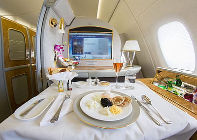 Emirates airlines first class suite with a large screen, a mini bar, and a table set with a meal and a drink in a glass flute.