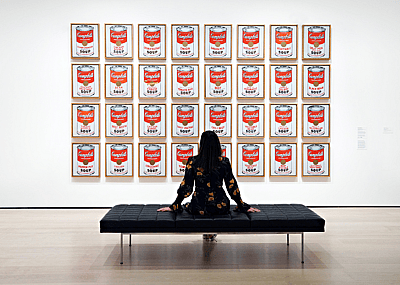 Person at MOMA sitting bench in front of Andy Warhol's 'Campbell's Soup Cans’.