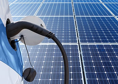 Close up of electric car with a connected charging cable on the background of solar panels.
