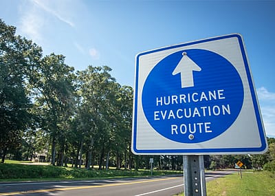 A hurricane evacuation route sign at the side of a gravel roadway.