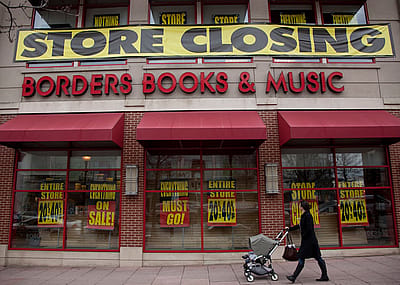 A person with a stroller walks by a "Store Closing" banner above a Borders Books & Music storefront.