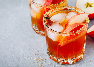 Closeup of apple cider cocktail with salt on the rim, apple slices, and ice.