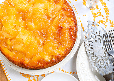 A gooey apple upside down cake on a white and orange towel with silver serving ware.