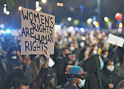 Image shows a rally of people with a person holding a sign that says "Women's rights are human rights"