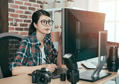 A woman with glasses looks intently at her monitor with camera equipment around her.