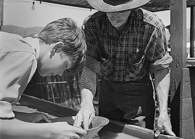 A man instructs a boy panning for gold at a 'Pan Your Own Gold' panning booth, costing 25 cents, with all proceeds going to the Western Mining Council, which promotes mining in Plumas County, California, circa 1950.