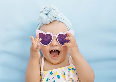 Baby wearing a turban and heart sunglasses on a blue background.