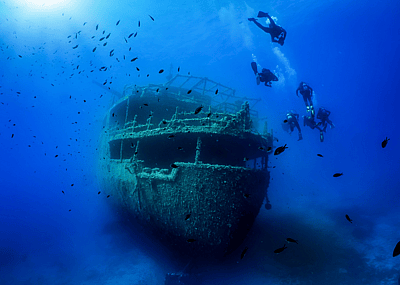 A group of divers explore a sunken shipwreck in the blue, Mediterranean sea at Naxos island, Greece