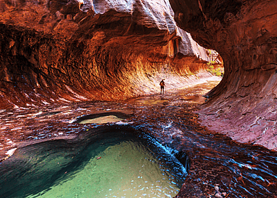 Hiker wading through the waters of the Narrows slot canyon in Zion National Park, Utah.