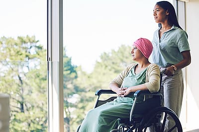 A woman in her 30s pushes another older woman in a wheelchair down a hallway.