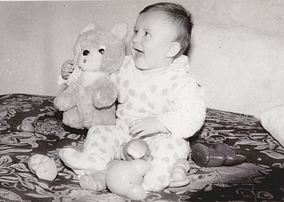 Old cute photo of a baby sitting with toys.
