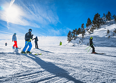 People skiing and snowboarding down a ski slope against a clear blue sky