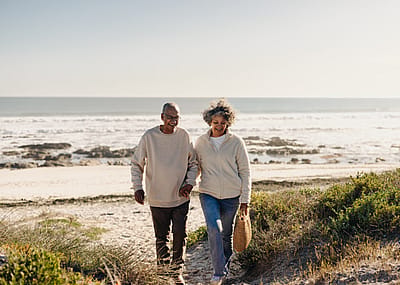 Cheerful elderly couple smiling happily while walking away from the beach after a picnic.