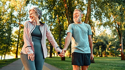 Modern active cheerful sports couple of senior people holding hands and talking cheerfully outdoors together.