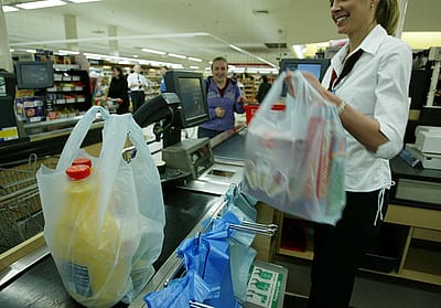 A smiling cashier at a grocery store bagging groeries.
